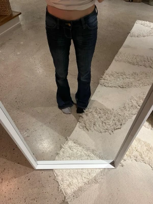 Mörkblå bootcut jeans från True Religion - Säljer ett par mörkblå bootcut jeans från cheap Monday i storlek 26/32 med klassiska kontrastsömmar och låg midja. Jeansen har helt vanliga bakfickor och . Perfekta för dig som gillar en avslappnad men snygg stil.