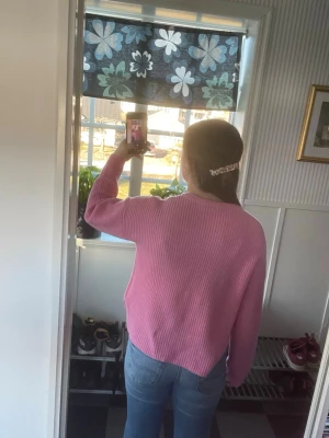 Rosa ribbstickad tröja - En söt rosa stickad tröja med ribbad struktur och rund hals. Tröjan har en avslappnad passform och långa ärmar. Perfekt för dig som gillar färg och vill ha något mjukt och bekvämt. Materialet ser ut att vara en mjuk bomulls- eller akrylblandning.