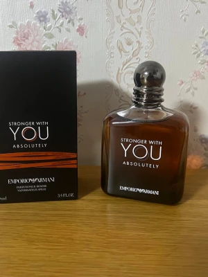 Emporio Armani Stronger With You Absolutely - Emporio Armani Stronger With You Absolutely är en parfym för honom med en elegant, mörkbrun glasflaska och silverfärgad rund kork. Flaskan har en stilren design med vit text och kommer i en svart kartong med orange detaljer. Doften är intensiv och modern.