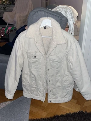 Vit jeansjacka med teddyfoder - Säljer en vit jeansjacka från H&M med mysigt teddyfoder och bred krage. Jackan har två bröstfickor med knapp och klassisk knappstängning framtill. Perfekt för dig som vill ha en stilren och trendig look.