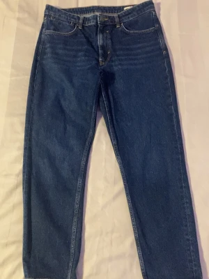 Mörkblå raka jeans - Säljer ett par mörkblå jeans med rak passform och klassisk femficksdesign. Jeansen har en hög midja och är tillverkade i denim. Perfekta för dig som gillar en tidlös och enkel stil.
