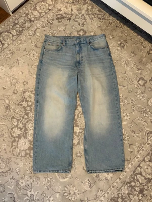 Ljusblå raka jeans med vintage-look - Säljer ett par ljusblå jeans med rak passform och snyggt slitna detaljer framtill och baktill. Jeansen har klassisk femficksdesign och är gjorda i kraftigt denimtyg. Perfekta för dig som gillar en avslappnad och trendig stil.
