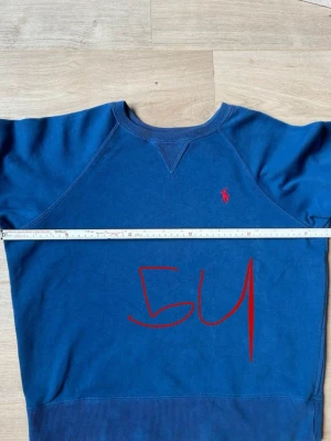 Blå crewneck från Ralph Lauren - Snygg blå crewneck från Ralph Lauren med klassisk röd logga broderad på bröstet. Tröjan har rund halsringning, ribbade muddar och nederkant samt raglanärmar för en avslappnad look. Perfekt till jeans eller sweatpants.