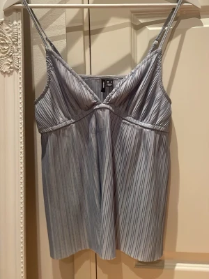 Ljusblå randig linnetopp Vero Moda - Säljer en ljusblå linnetopp från Vero Moda med tunna axelband och vertikala ränder. Toppen har en v-ringad skärning och är tillverkad i ett mjukt, lätt material som passar perfekt till sommaren. Enkel och stilren design som är lätt att matcha.