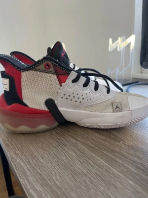 Jordan Why Not Zer0.3 sneakers - Snygga Jordan Why Not Zer0.3 sneakers i vitt, rött och svart. Ovandelen är i mesh och syntet med coola detaljer och perforeringar. Sulan är vit med röda och svarta inslag och har ett tydligt Jordan-logga på sidan. Perfekta för dig som gillar basketstil. Priset är diskuterbart!!
