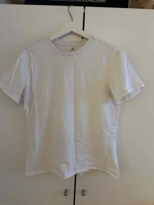 Vit basic t-shirt från H&M - En klassisk vit t-shirt från H&M med rund hals och korta ärmar. Tillverkad i mjuk bomull som känns skön mot huden. Perfekt att matcha med jeans eller shorts för en enkel och clean look.
