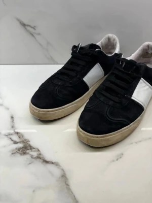 Svarta och vita sneakers i mocka - Säljer ett par svarta sneakers med vita detaljer och beige sula. Skorna har en klassisk låg profil och är tillverkade i mocka med snörning framtill. Perfekta för dig som gillar stilrena och tidlösa sneakers märke valentino. Och ett par vita valentino opens 
