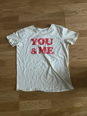 Vit t-shirt med röd text - Vit t-shirt med trycket 'YOU & ME' i röd på bröstet. Klassisk rund halsringning och korta ärmar. Perfekt för en avslappnad och trendig stil.
