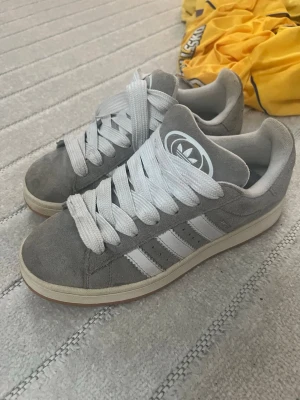 Grå Adidas campus 00s - Snygga grå Adidas campus 00s. Skorna har låg profil och är gjorda i mockaliknande material med gummisula. Perfekta för en avslappnad streetstyle-look.