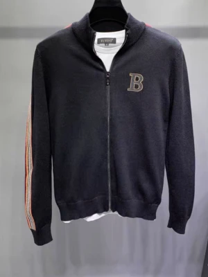 Burberry tröja  - Snygg svart ziptröja från burberry med broderad B på bröstet. Tröjan har färgglada ränder i rött, vitt och beige längs ärmarna och ribbade muddar. Perfekt för en sportig och avslappnad stil.