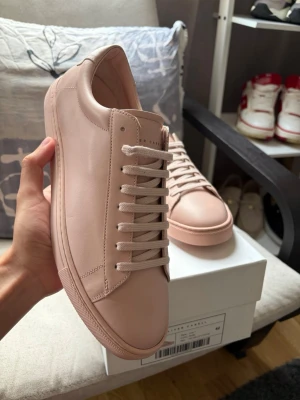 Ljusrosa sneakers från Oliver Cabell - Stilrena ljusrosa sneakers från Oliver Cabell  i slätt läder. Klassisk låg modell med matchande snörning och sula. Diskret guldprägling på sidan och minimalistisk design som passar till det mesta. Perfekta för dig som gillar clean och modern stil.