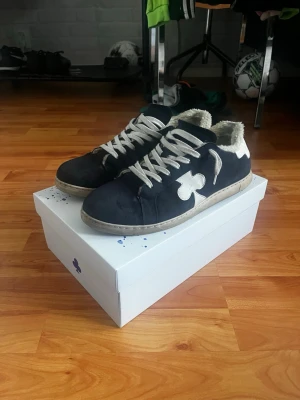 Svarta sneakers från The Galleryist - Mörkblåa skor från The Gallerist med vit sula och vita skosnören. Skorna har en vit klöverdetalj på sidan och mjukt, luddigt foder på insidan för extra komfort. Klassisk låg modell som passar till många stilar. Tvättas självklart innan den fraktas!!! Tveka inte på frågor eller funderingar!!