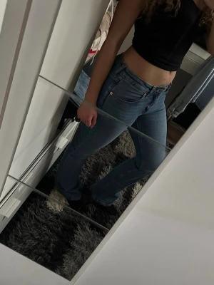 Blå bootcut jeans med hög midja - Säljer ett par ljusblå bootcut jeans med hög midja och klassisk femficksdesign. Jeansen har en snygg tvätt och raka ben som går ut lite nedtill. Perfekta till crop tops och sneakers för en chill look.