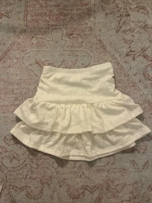 Vit blommig kjol med volanger - Supersöt vit skort med blommigt mönster och dubbla volanger. inbyggda shorts i mjuk bomull. Perfekt för dig som vill ha kjol-looken men ändå känna dig bekväm