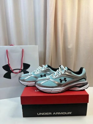 Under Armour blå sneakers mesh - Snygga sneakers från Under Armour i ljusblå mesh med silverfärgade detaljer och vita skosnören. Skorna har svart logga på sidan och svart insida. Sulan är vit med svarta och grå inslag. Perfekta för dig som gillar sportig och modern stil.