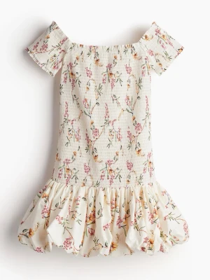 Blommig offshoulder kortklänning - Söt kortklänning med offshoulder och volangkant. Klänningen är vit med blommigt mönster i rosa, grönt och gult. Den är insydd i midjan, kontakta för fler bilder 