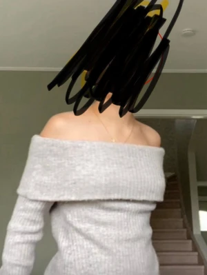 Ljusgrå off shoulder stickad tröja - Trendig ljusgrå stickad tröja med bred off shoulder-krage och långa ärmar. Tröjan har en ribbad struktur och sitter figurnära för en snygg siluett. Perfekt att styla med jeans eller kjol för en cool look.