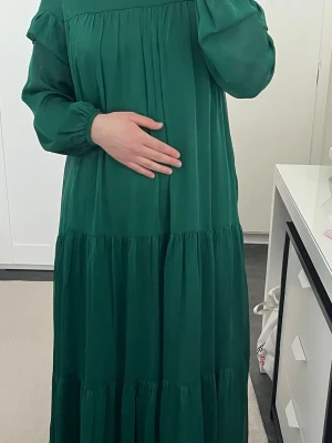 Grön långklänning med volang - Säljer en grön långklänning med volangdetaljer och långa ärmar. Klänningen har en lös passform och är tillverkad i ett mjukt, lätt tyg som ger ett fint fall. Perfekt för dig som gillar en avslappnad men ändå stilren look.