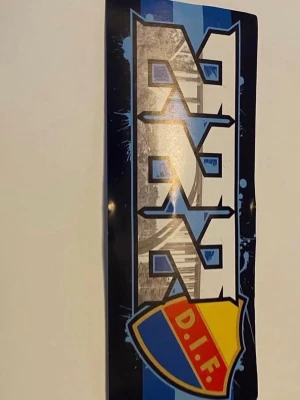 Sofialäktaren Dif - Säljer ett klistermärke med Djurgårdens IF:s logotyp i blått, gult och rött. Motivet har en grafisk text och bakgrund i blåa nyanser med inslag av vitt och svart. Perfekt för att dekorera laptop, vägg eller andra ytor.
