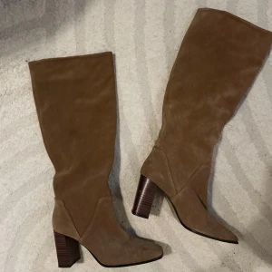 Bruna höga mockastövlar med klack - Snygga knähöga stövlar från Mango Brun/beige färg i äkta mocka och helt oanvända.  Storlek: 39 Stabil blockklack, bekväma att gå i.