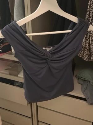 Mörkblå offshoulder topp med twist - Snygg mörkblå offshoulder topp med twistad detalj framtill. Toppen är ärmlös och har en smickrande v-ringning.