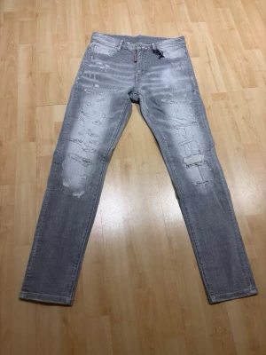 Grå slitna skinny jeans - Säljer ett par grå skinny jeans med slitningar och distressed detaljer på både fram- och baksida. Jeansen har klassisk femficksmodell och dragkedjegylf. Perfekta för dig som gillar en trendig och avslappnad stil.