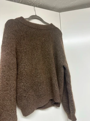 Brun stickad tröja från Lindex - Mysig brun stickad tröja från Lindex med rund halsringning och ribbade muddar. Tröjan har en lätt luddig yta och är perfekt för kyliga dagar. Enkel och stilren design som passar till det mesta.