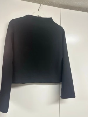 Svart tröja från Visual Clothing Project - En stilren svart tröja från Visual Clothing Project i storlek XS. Tröjan har en rak passform, långa ärmar och enkel design utan synliga detaljer. Perfekt för dig som gillar minimalistisk stil.