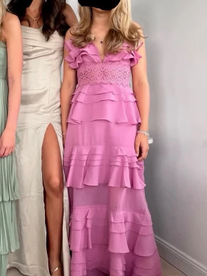 Lång rosa volangklänning med spets - Super fin lila/rosa balklänning i mycket bra skick. Uppsydd dvs lite kortare än originalet men inget som syns över huvud taget. Minimal defekt se bild. Storlek 6, sitter som xs.