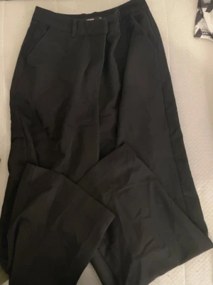 Svarta kostymbyxor från bik bok - Säljer ett par svarta kostymbyxor från bik bok med raka ben och pressveck. Byxorna har fickor i sidorna och hällor för skärp. Perfekta för en clean och stilren look.