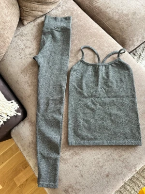 Grått träningsset med linne & tights - Säljer ett grått  set med linne och matchande tights. Linnet har smala axelband och tightsen är höga i midjan. Materialet är stretchigt och mjukt, perfekt för en bekväm känsla. Passar dig som gillar stilrena och enkla träningskläder. Passar S M L. Nypris 1499kr