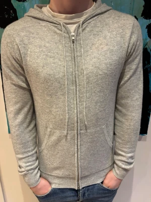 Ljusgrå zip 100% kashmirhoodie - Snygg ljusgrå 100% Kashmirhoodie med dragkedja framtill och två fickor. Nypris 2999 kr | Mitt pris 1599 Perfekt till jeans och enkel att matcha med andra plagg. Skicket är som ny.