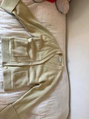 ❤️Beige kofta från & other stories ❤️ - Mysig beige kofta från &other stories med v-ringning och stora ribbade muddar. Koftan har två rejäla framfickor och stängs med fyra matchande knappar. Tillverkad i mjukt stickat material som känns lyxigt och skönt. Använd en gång och ny.