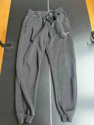 Svarta mjukisbyxor från Björn Borg - Säljer ett par svarta mjukisbyxor från Björn Borg med logga på vänster ben. Byxorna har dragsko i midjan, ribbade muddar vid benslut och sidofickor. Perfekta för chill eller träning, tillverkade i mjukt material som känns skönt mot huden.