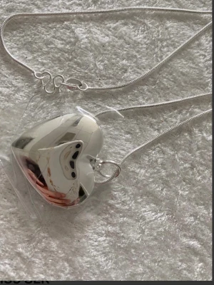 Silverfärgat hjärthalsband från Avon - Snyggt halsband i silverfärg med ett hjärtformat hänge som går att öppna. Halsbandet har en tunn kedja och hjärtat har en blank, spegelblank yta. Perfekt accessoar för att ge din outfit en personlig touch.