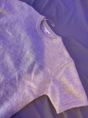 Beige stickad tröja från Gina Tricot - Mysig beige stickad tröja från Gina med rund halsringning och korta ärmar. Tröjan har en enkel och clean design, perfekt för lager på lager och chill vardagsstil. 