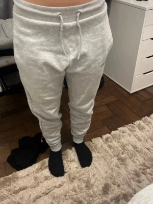 Ljusgrå mjukisbyxor med dragsko - Säljer ett par ljusgrå mjukisbyxor med dragsko i midjan och muddar vid bensluten. Byxorna har en avslappnad passform och är tillverkade i mjukt sweatshirtmaterial. Perfekta för chill dagar hemma eller när du vill vara bekväm. Färg på byxorna går inte bort 