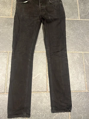 Nudie Jenas  - Säljer ett par svarta slim fit jeans från Nudie Jeans. Jeansen har klassisk femficksmodell, raka ben och diskreta sömmar. Materialet är mjukt och stretchigt, vilket gör dem riktigt sköna att bära. Perfekta för dig som gillar en clean och stilren look. Modell: Grim Tim fint skick sparsamt använda. Storlek 30W 32 L 