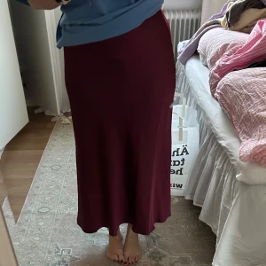 Vinröd långkjol i satin - Säljer en vinröd långkjol med enkel och stilren design. Kjolen har en lätt utsvängd form. Använd en gång så den är i nyskick❤️