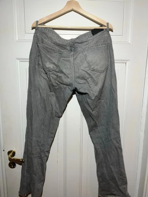 Grå raka jeans med rå kant - Säljer ett par grå jeans med rak passform och rå, fransig kant nedtill. Jeansen har klassisk femficksdesign och knappgylf. Perfekta för en avslappnad och trendig look.