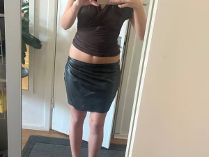 Skin kjol - Säljer en svart kort kjol i skinnimitation med en clean och stilren look. Kjolen har en tight passform och sitter högt i midjan. Perfekt att matcha med en crop top eller oversized tröja för en trendig outfit. Ny