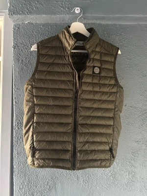 Olivgrön dunväst från Stone Island - Snygg olivgrön dunväst från Stone Island🫒 med quiltad design och hög krage. Västen har dragkedja framtill, två sidofickor med dragkedja och den klassiska Stone Island-loggan på bröstet. Perfekt för lager-på-lager. Perfekt nu inför våren! Passar mig fortfarande perfekt som 173 cm kan enkelt passa upp till 175-180😃