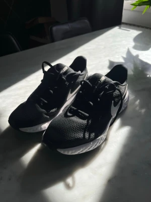 Svarta Nike sneakers med vit sula - Snygga svarta Nike sneakers med vit sula och klassisk swoosh på sidan. Ovandelen är i mesh för bra andningsförmåga och skorna har svarta skosnören. Perfekta för dig som gillar sportig och stilren look.