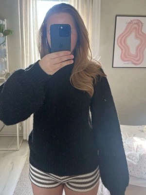 Svart stickad tröja med ballongärm - Mysig svart stickad tröja med ballongärmar och ribbade muddar vid ärmslut och nederkant. Tröjan har en klassisk rund halsringning och är perfekt för lager-på-lager-stil. Materialet ser ut att vara ullblandning.