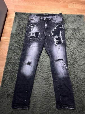 Supply demand byxor - Säljer ett par svarta skinny jeans från Only & Sons med kraftiga slitningar, hål och patchade detaljer framtill. Jeansen har en tvättad look, fem fickor och råa benslut. Materialet är bomull med stretch för skön passform.