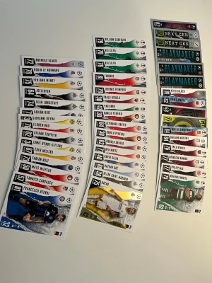 Samling fotbollskort CHL, EL, COL - Säljer en samling fotbollskort från UEFA CHL, EL, COL med olika spelare och specialkort som Playmaker och Next Gen. Korten har färgstarka designer och visar spelare i matchställ från flera kända klubbar. Perfekt för dig som gillar att samla sportkort eller vill byta med vänner. 48 kort 