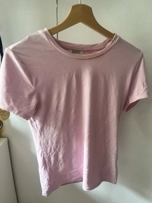 Ljusrosa basic t-shirt - En enkel och stilren ljusrosa t-shirt med rund hals och korta ärmar. Perfekt att matcha med jeans eller shorts för en avslappnad look. Tillverkad i mjuk bomull som känns skön mot huden.(Det finns en liten fläck på ryggen men syns inte så mycket )