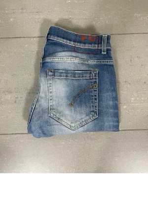 Dondup George jeans - Säljer ett par blå slim fit jeans med snygga slitningar och tvättade detaljer. Jeansen har klassiska fem fickor och kontrastsömmar. Perfekta för en avslappnad och trendig look.