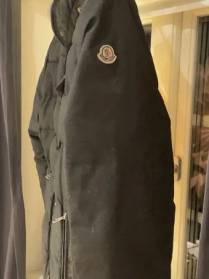Svart dunjacka från Moncler - Snygg svart dunjacka från Moncler med klassisk patch på ärmen och dragkedja framtill. Jackan har hög krage och quiltad design som ger en modern look. Perfekt för kalla vinterdagar och riktigt varm tack vare dunfyllningen. ❗️PRIS KAN DISKUTERAS DÅ JACKAN ÄR FÖR LITEN❗️