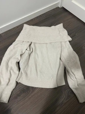 Offwhite stickad tröja från Newyorker  - Säljer en offwhite stickad tröja från Newyorker som är offshoulder och långa ärmar. Tröjan har ribbade muddar vid ärmslut och nederkant, och är gjord i ett mjukt stickat material. Den är i storlek 38.